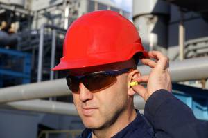 worker with red hard hat putting earplug in