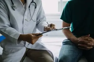 doctor sitting on patient table with clipboard talking to patient. No faces